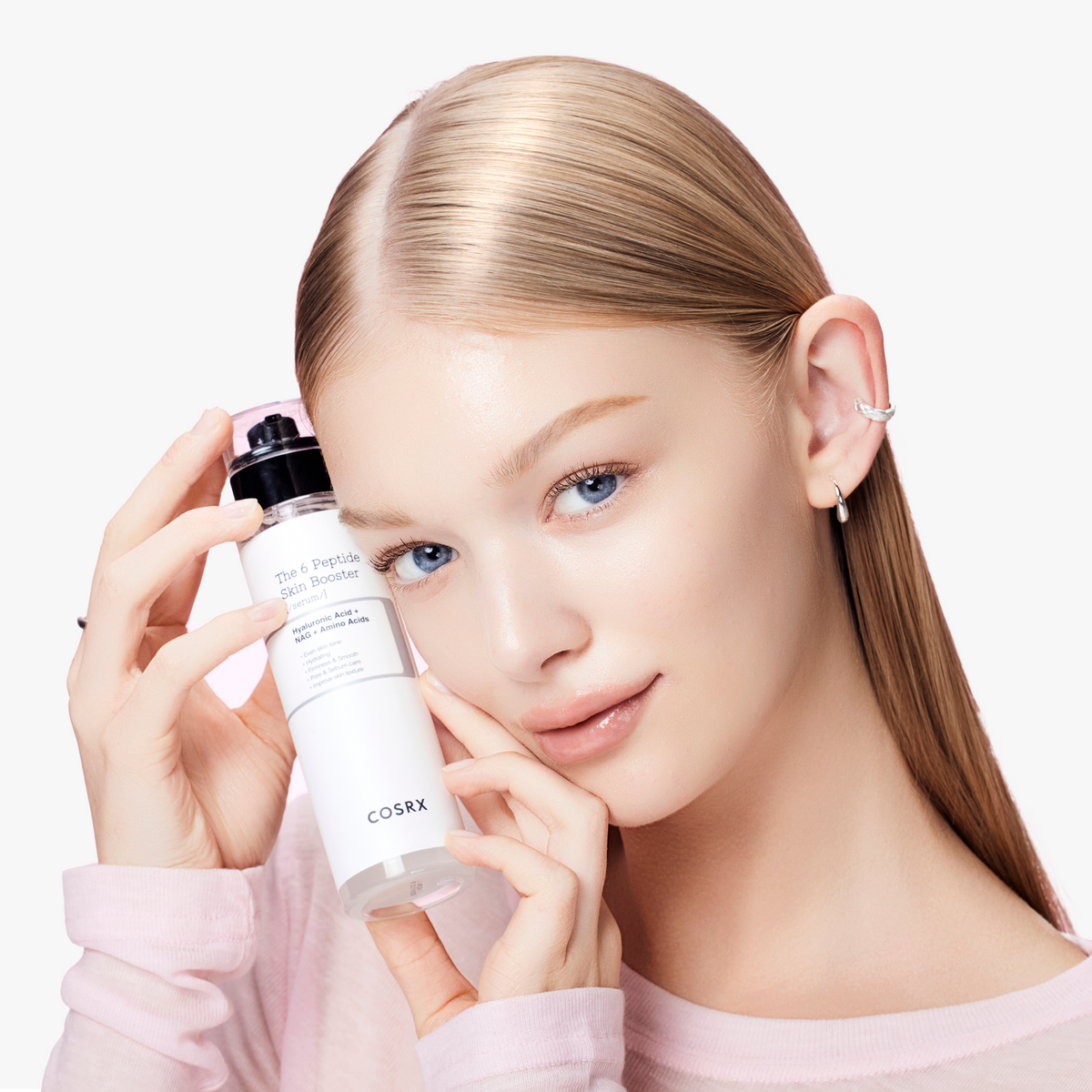 Model with luminous, even-toned skin holding COSRX The 6 Peptide Skin Booster Serum near her face; Korean first-step all-in-one serum infused with six peptides, hyaluronic acid, and amino acids to enhance firmness, glow, and hydration while supporting sensitive skin and slow-aging care.