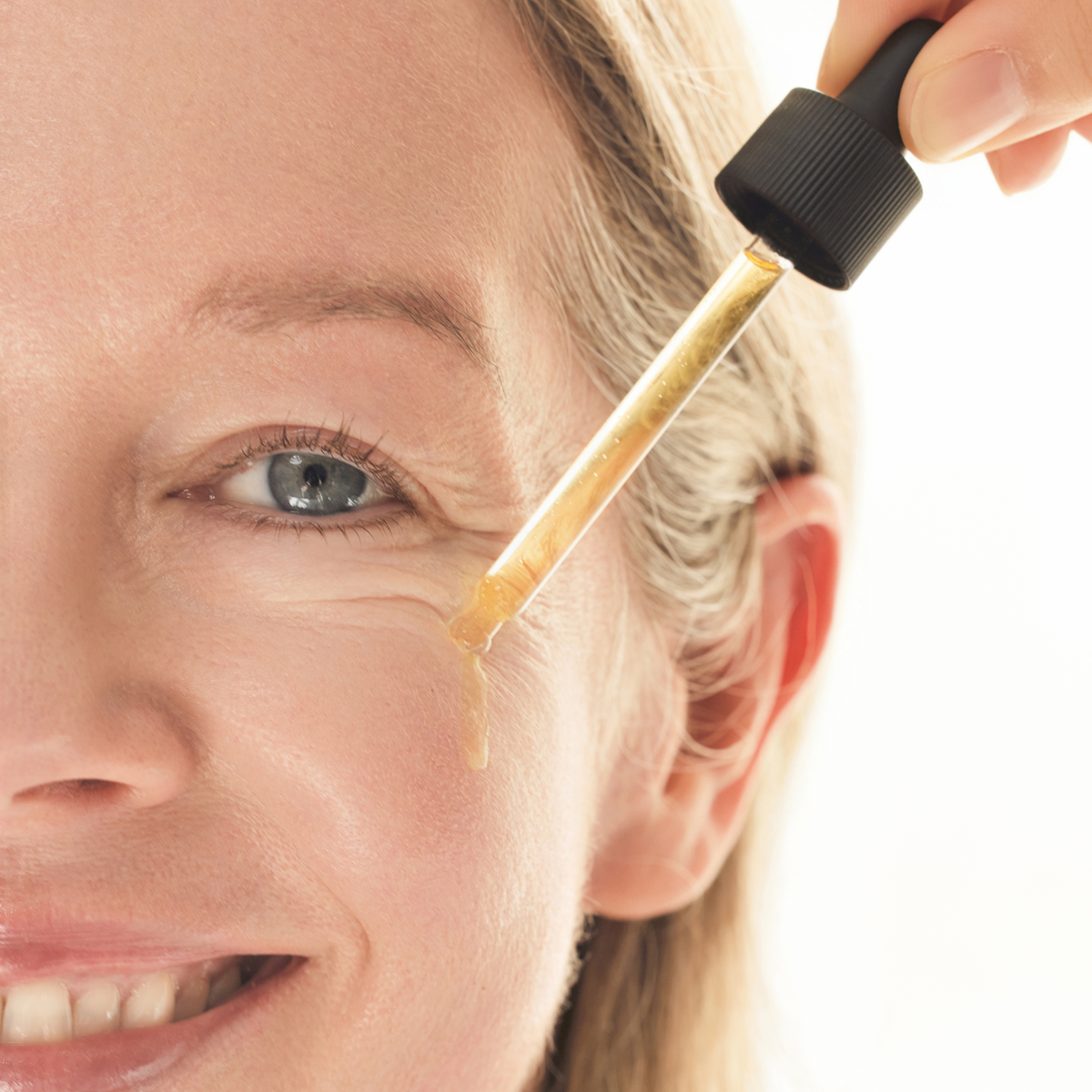 Close-up of mature model applying COSRX Advanced The Vitamin C 23 Serum near the eye contour; antioxidant-rich Vitamin C and E complex visibly smooths fine lines, reduces wrinkles, and evens tone for firmer, brighter skin. Clinically shown to improve elasticity and reduce pore volume by 38.15% after 4 weeks of consistent use.