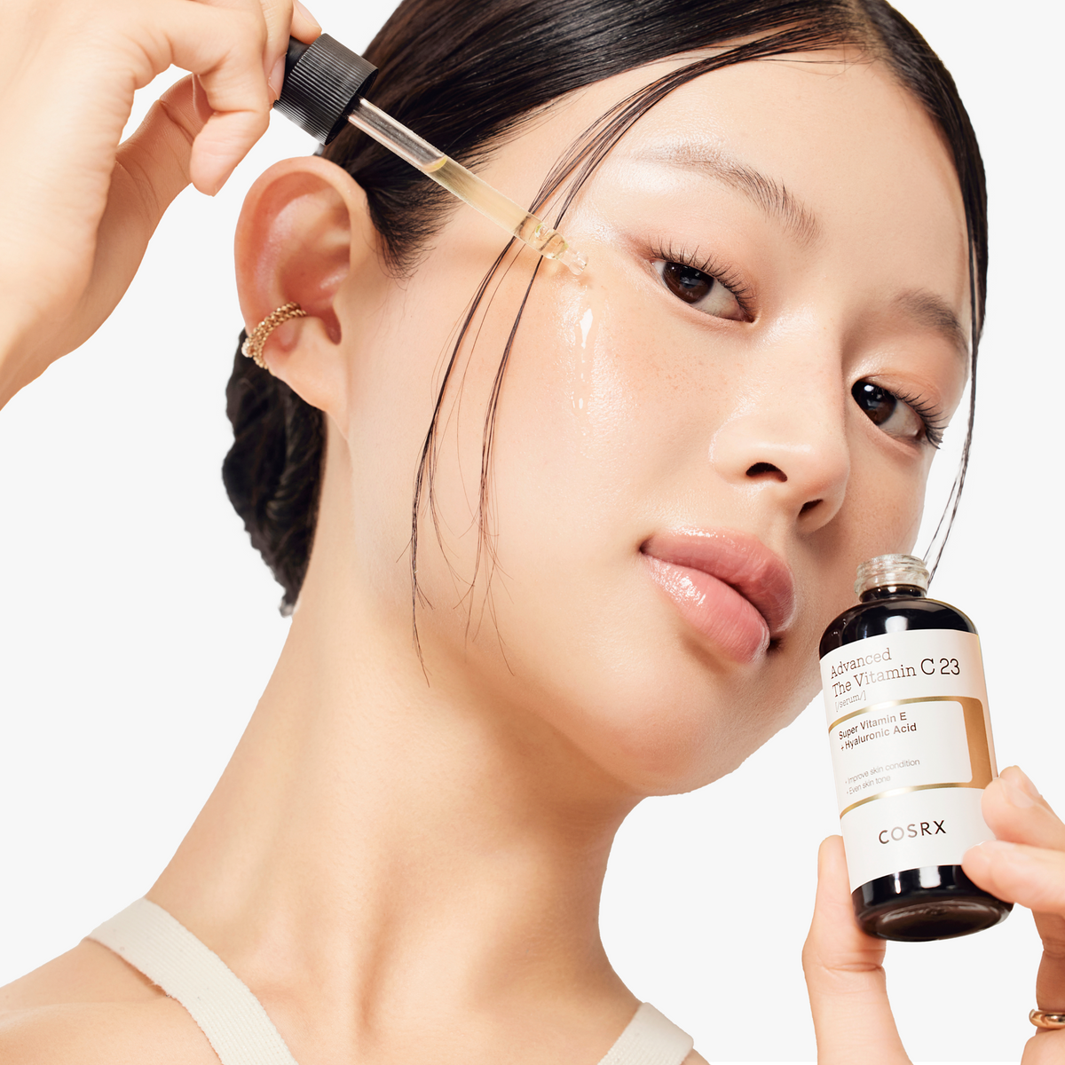 Model applying COSRX Advanced The Vitamin C 23 Serum with a luminous glow; dual-layer formula of stabilized Vitamin C and Hyaluronic Acid deeply hydrates, brightens dull areas, and refines uneven texture for a smooth, radiant finish. Clinically proven to reduce five types of blemishes by 30.14% after 4 weeks of use.