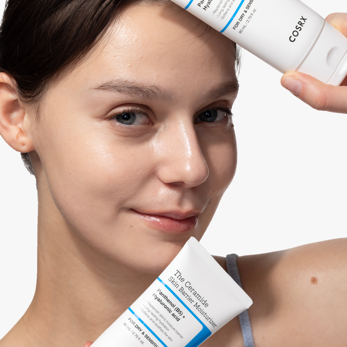 Smiling model applying COSRX The Ceramide Skin Barrier Moisturizer while holding the tube, showcasing its lightweight creamy texture during a daily skincare routine. Enriched with Ceramides, Cholesterol, Fatty Acids, Panthenol (B5), and 5 types of Hyaluronic Acid, this Korean moisturizer strengthens the skin barrier, deeply hydrates, and soothes dryness, making it ideal for smooth, glowing skin prep before makeup.