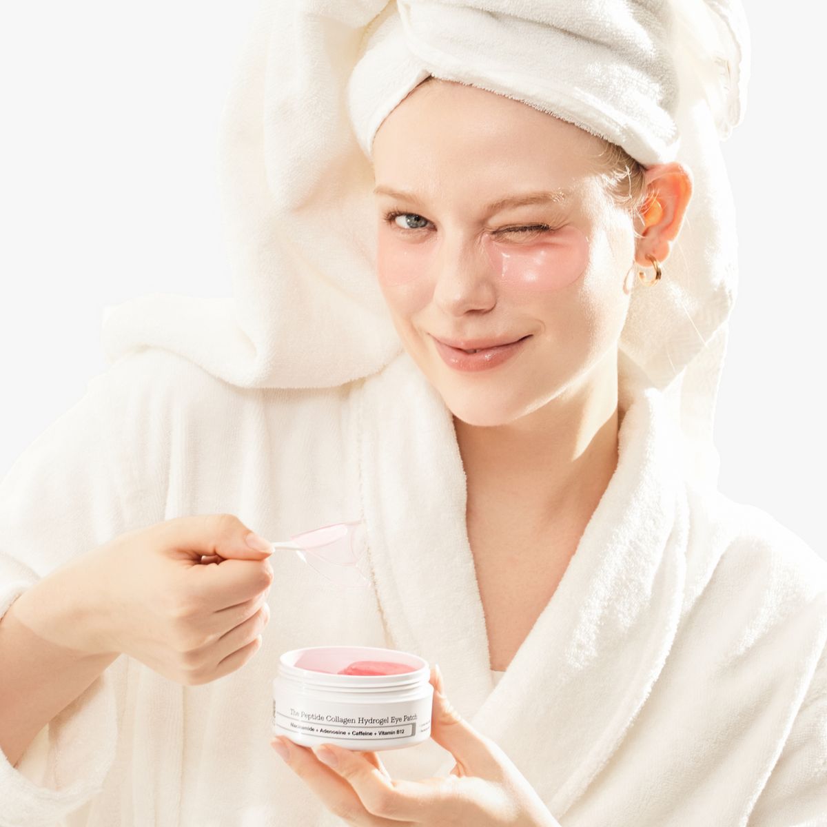 Model in white robe using spatula to apply COSRX The Peptide Collagen Hydrogel Eye Patch; lighthearted skincare moment showcasing pink peptide-infused hydrogel eye patches clinically proven to reduce puffiness, smooth the appearance of fine lines, and hydrate sensitive under-eye skin.
