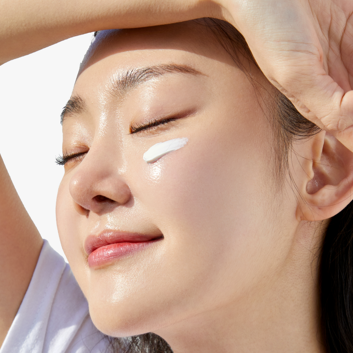 Sunlit close-up of model wearing COSRX Vitamin E Vitalizing Sunscreen SPF 50+ with visible product swipe on cheek; illustrates luminous, hydrated finish without white cast, ideal for sensitive skin and daily use under makeup.